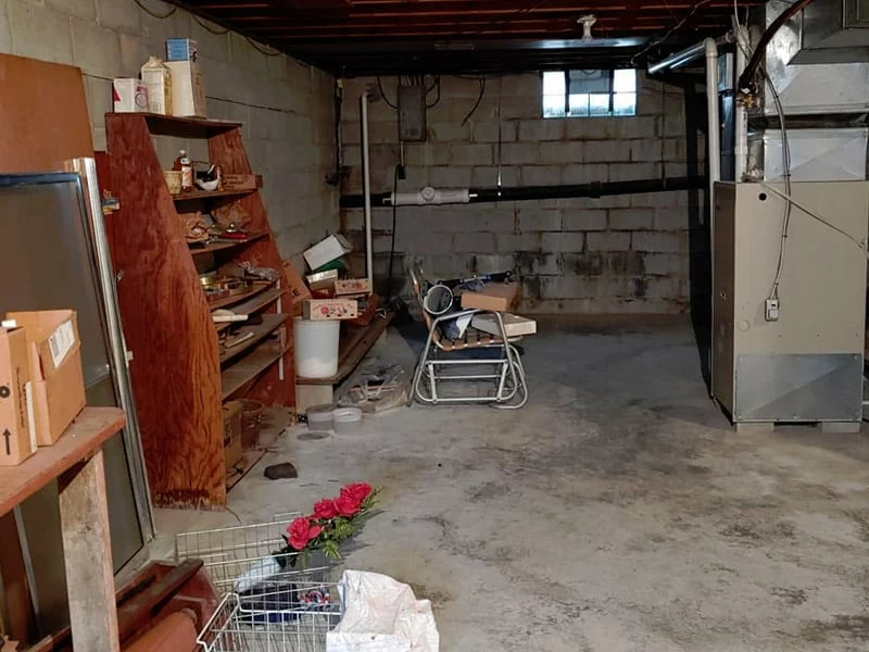 Cave encombrée de meubles, d’étagères et de cartons avant intervention